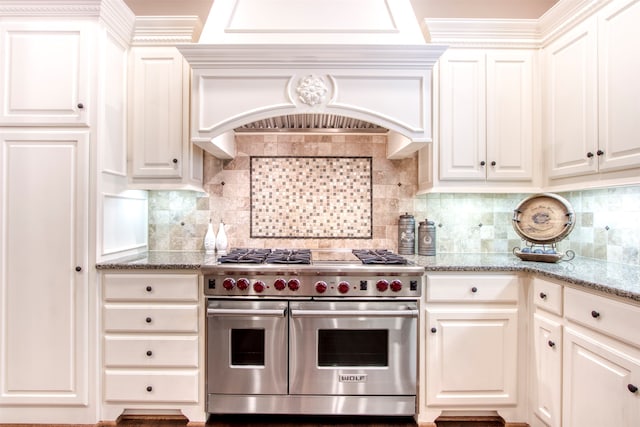 kitchen featuring light stone counters, decorative backsplash, range with two ovens, white cabinets, and custom exhaust hood