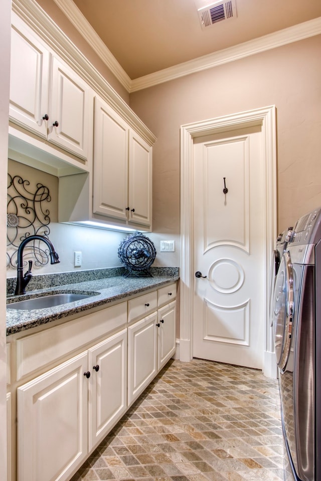 clothes washing area with ornamental molding, washer and clothes dryer, cabinets, and sink