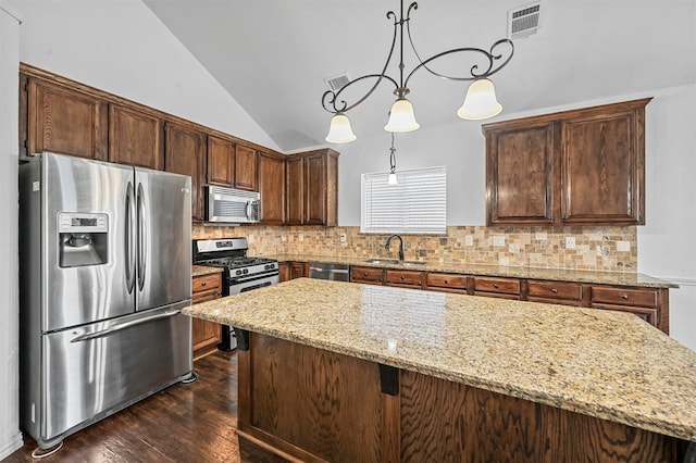 kitchen with appliances with stainless steel finishes, sink, decorative light fixtures, dark wood-type flooring, and light stone counters