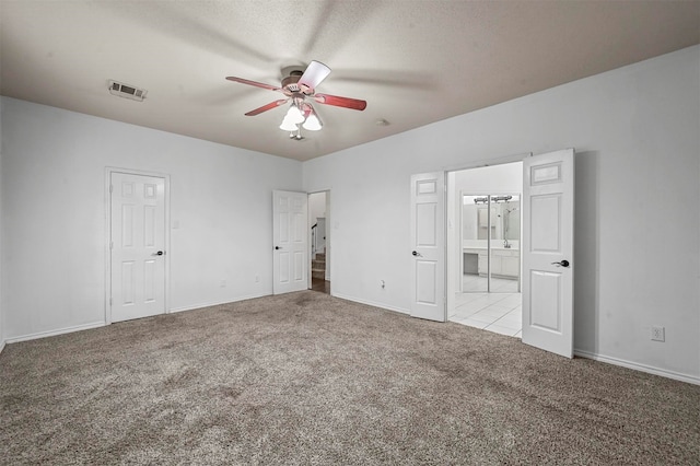 unfurnished bedroom featuring ceiling fan, ensuite bath, a textured ceiling, and light colored carpet