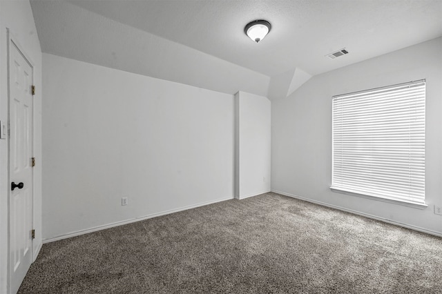 empty room featuring dark carpet, vaulted ceiling, and a textured ceiling