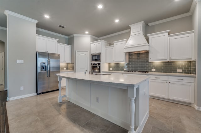 kitchen featuring white cabinetry, stainless steel appliances, premium range hood, sink, and a center island with sink