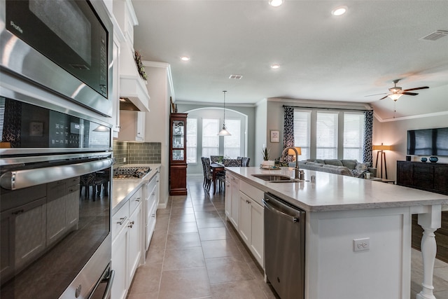 kitchen featuring decorative light fixtures, appliances with stainless steel finishes, white cabinetry, and a center island with sink