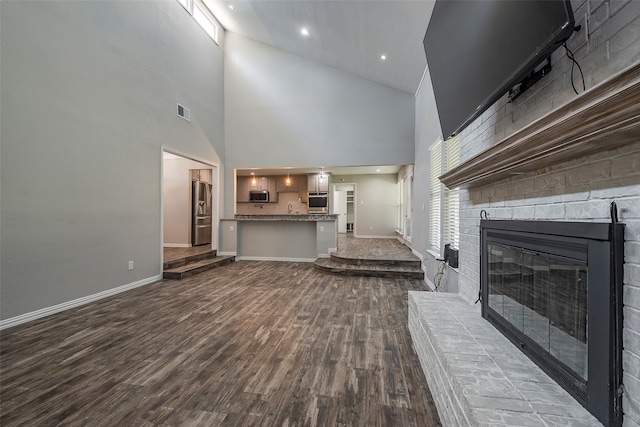 unfurnished living room featuring high vaulted ceiling, wood-type flooring, and a brick fireplace