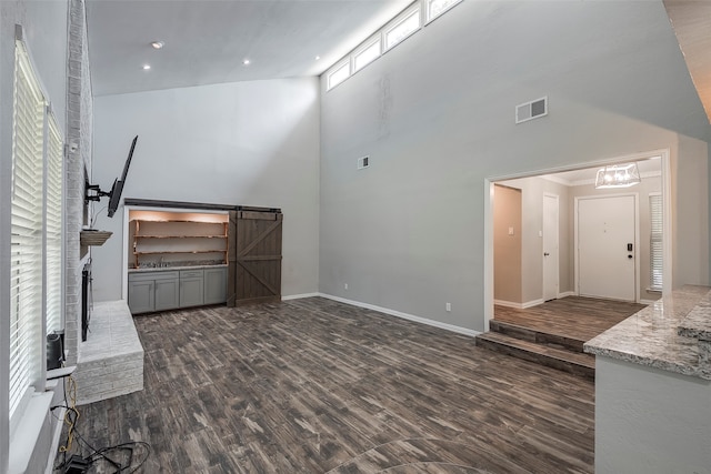 unfurnished living room with a barn door, dark hardwood / wood-style floors, and high vaulted ceiling