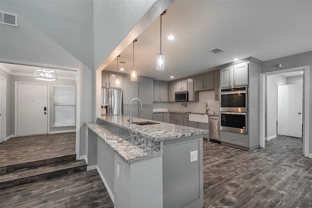 kitchen featuring appliances with stainless steel finishes, sink, kitchen peninsula, hanging light fixtures, and dark wood-type flooring