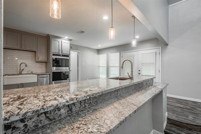 kitchen featuring sink, stainless steel double oven, pendant lighting, decorative backsplash, and dark hardwood / wood-style floors