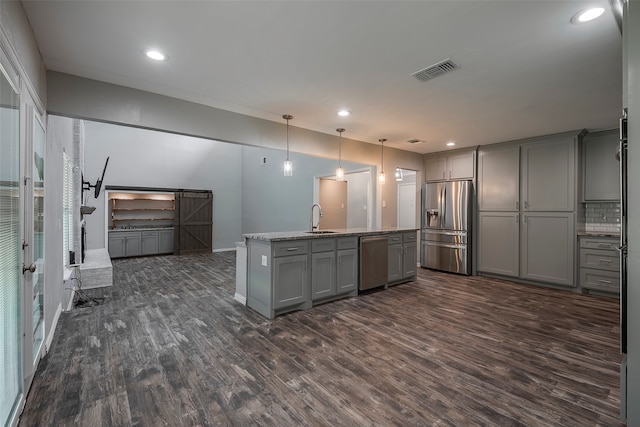 kitchen with dark hardwood / wood-style flooring, appliances with stainless steel finishes, a barn door, gray cabinets, and decorative light fixtures