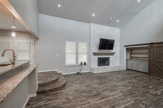 living room featuring dark hardwood / wood-style floors, a barn door, high vaulted ceiling, and a fireplace