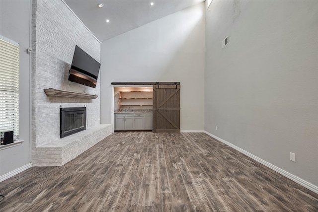 unfurnished living room with dark wood-type flooring, high vaulted ceiling, a fireplace, and a barn door