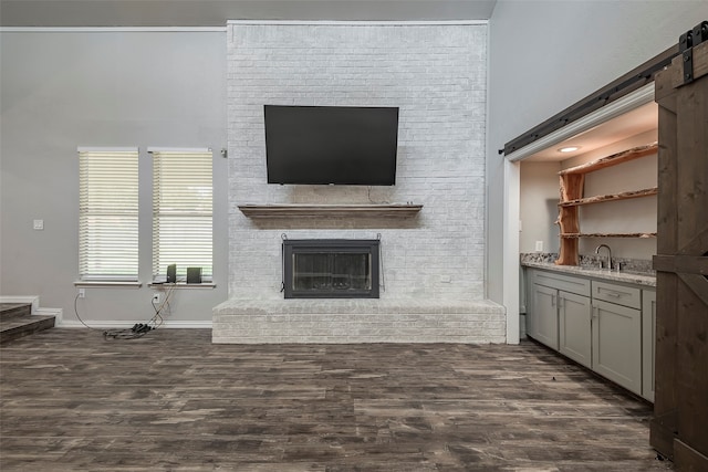 unfurnished living room featuring sink, a barn door, dark hardwood / wood-style flooring, and a fireplace