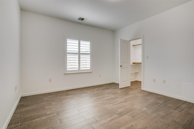 unfurnished bedroom featuring baseboards, wood finished floors, visible vents, and a walk in closet