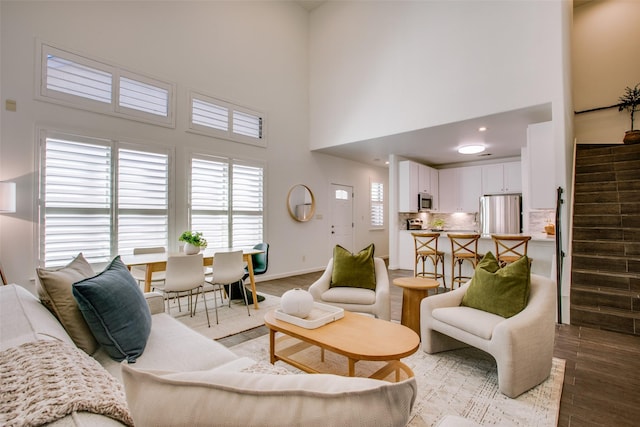 living area with a towering ceiling, stairs, baseboards, and wood finished floors