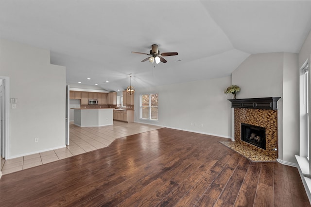 unfurnished living room featuring ceiling fan with notable chandelier, lofted ceiling, light wood-type flooring, and a fireplace