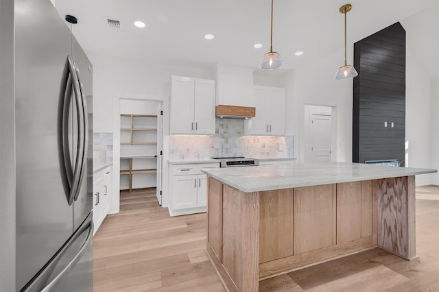 kitchen featuring a kitchen island, white cabinetry, stainless steel refrigerator, and light stone counters