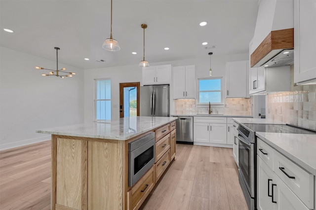 kitchen featuring a kitchen island, decorative light fixtures, stainless steel appliances, and white cabinets