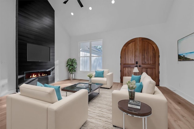 living room featuring light hardwood / wood-style floors, high vaulted ceiling, ceiling fan, and a large fireplace