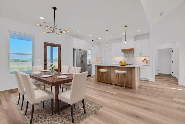 dining space with light wood-type flooring, sink, and an inviting chandelier