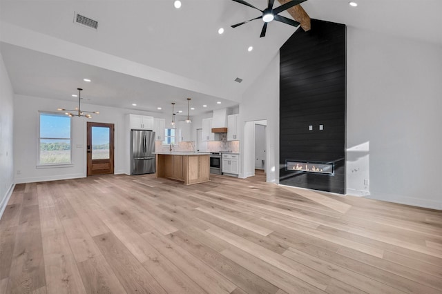 unfurnished living room with a fireplace, beamed ceiling, light wood-type flooring, and ceiling fan with notable chandelier