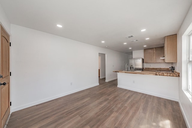 kitchen featuring dark wood-type flooring, stainless steel fridge with ice dispenser, kitchen peninsula, and light brown cabinets