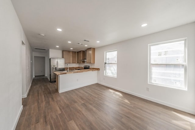 kitchen with appliances with stainless steel finishes, sink, kitchen peninsula, a kitchen breakfast bar, and dark wood-type flooring