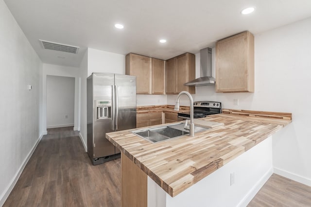 kitchen with butcher block countertops, stainless steel appliances, wall chimney exhaust hood, and dark hardwood / wood-style floors