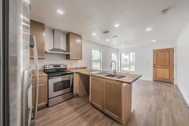 kitchen featuring wall chimney range hood, dark wood-type flooring, kitchen peninsula, sink, and appliances with stainless steel finishes