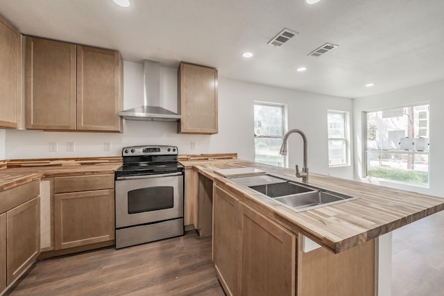 kitchen featuring butcher block counters, wall chimney range hood, a center island with sink, sink, and stainless steel range with electric cooktop