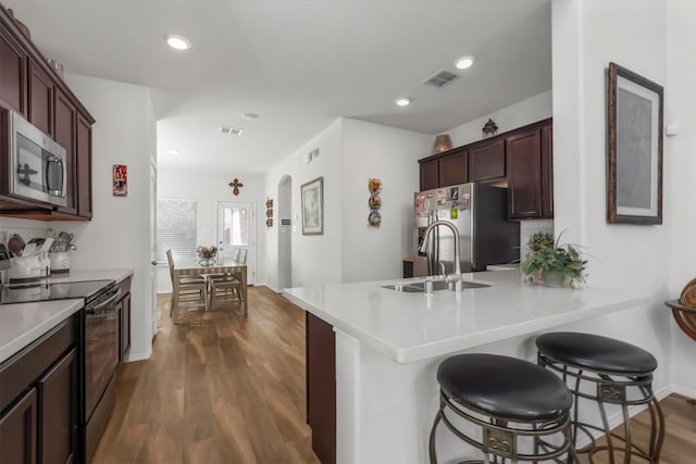 kitchen with sink, kitchen peninsula, stainless steel appliances, a breakfast bar, and dark hardwood / wood-style floors