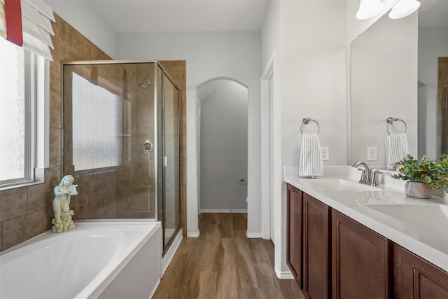 full bathroom with double vanity, a bath, a shower stall, wood finished floors, and a sink