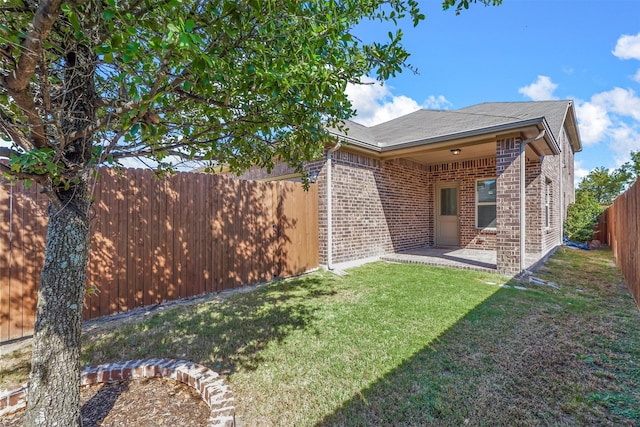 back of house featuring a patio, a fenced backyard, roof with shingles, brick siding, and a lawn