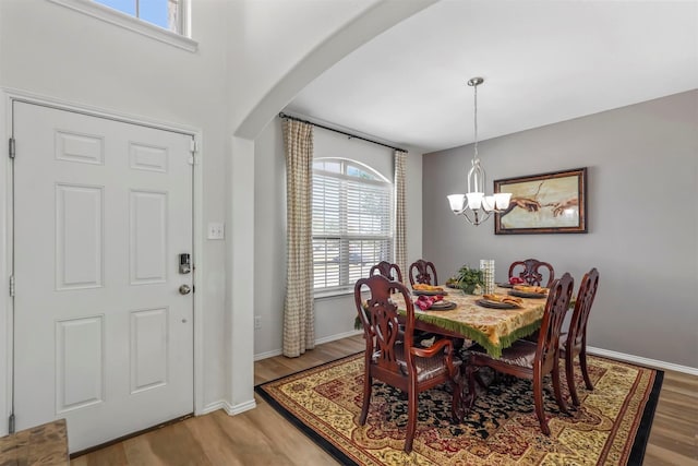 dining room featuring arched walkways, baseboards, an inviting chandelier, and light wood-style flooring