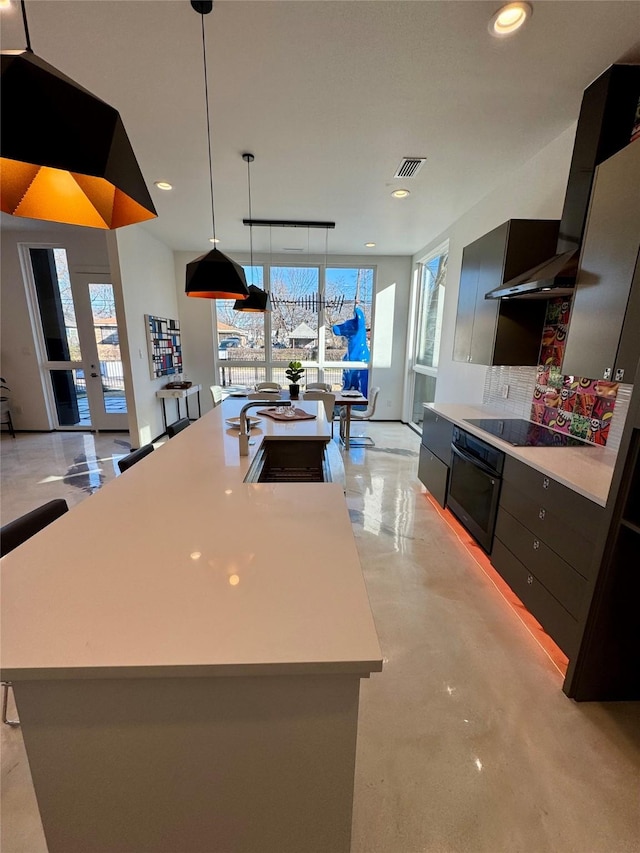 kitchen with sink, tasteful backsplash, black electric stovetop, decorative light fixtures, and a large island with sink