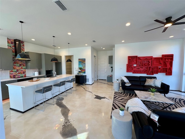 kitchen with gray cabinetry, backsplash, a kitchen bar, exhaust hood, and a center island with sink