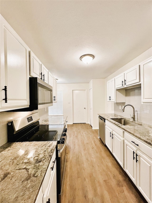 kitchen with sink, white cabinets, light wood-type flooring, appliances with stainless steel finishes, and light stone counters