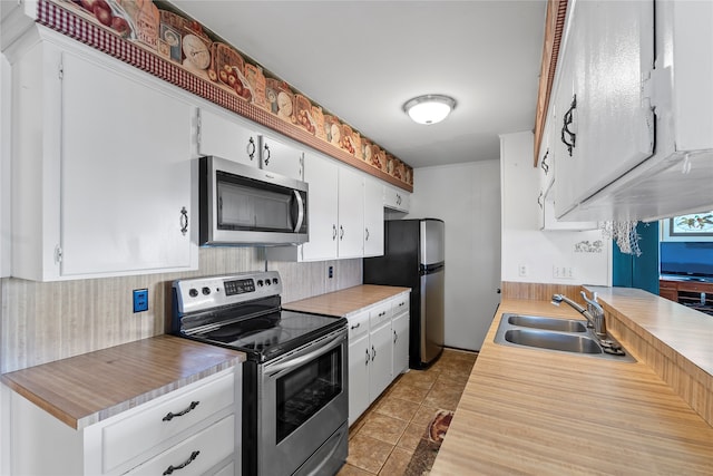 kitchen with appliances with stainless steel finishes, white cabinetry, light tile patterned flooring, and sink