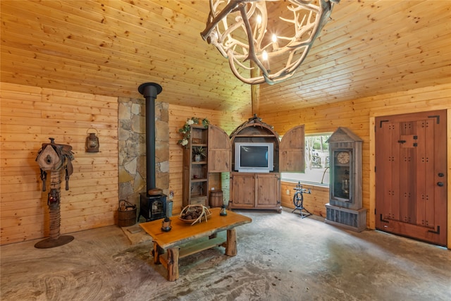 unfurnished living room with wooden walls, concrete floors, a wood stove, an inviting chandelier, and high vaulted ceiling