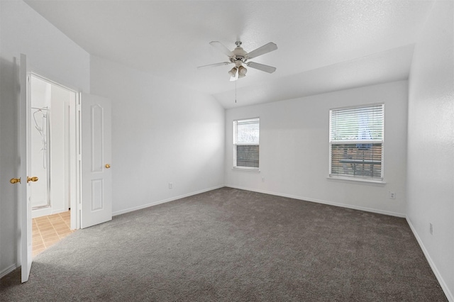 spare room with ceiling fan, vaulted ceiling, and dark colored carpet