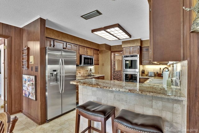 kitchen featuring kitchen peninsula, appliances with stainless steel finishes, backsplash, a breakfast bar, and sink