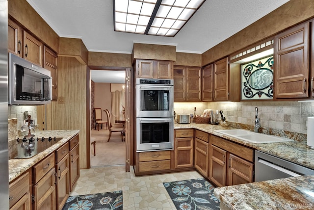 kitchen with light stone countertops, crown molding, sink, and stainless steel appliances