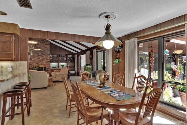 dining space featuring a brick fireplace, a textured ceiling, light tile patterned floors, lofted ceiling, and wood walls