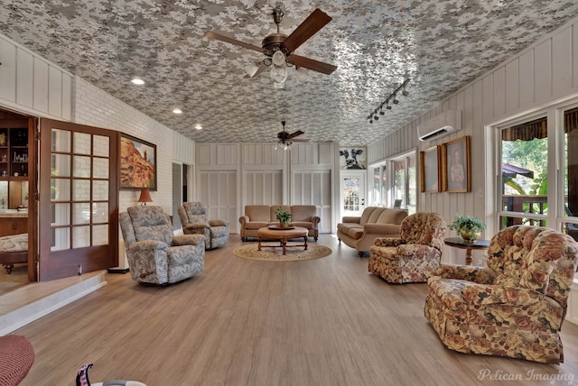 living room featuring a wall mounted AC, ceiling fan, wooden walls, and light wood-type flooring