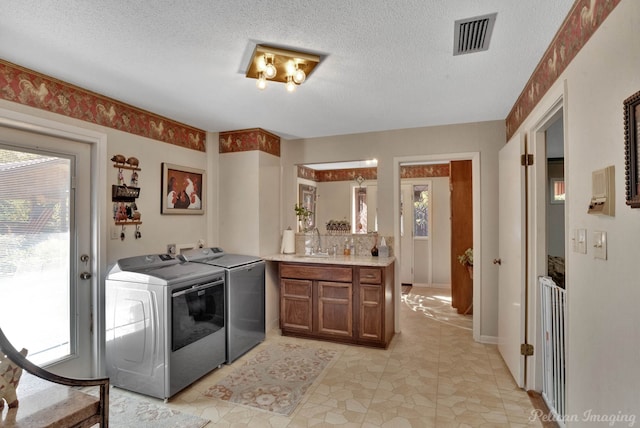 washroom with a textured ceiling, a healthy amount of sunlight, sink, and washing machine and clothes dryer