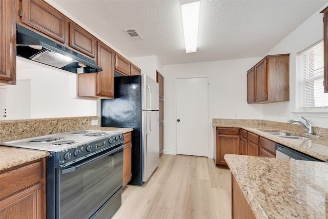 kitchen featuring light stone counters, appliances with stainless steel finishes, a textured ceiling, light hardwood / wood-style floors, and sink