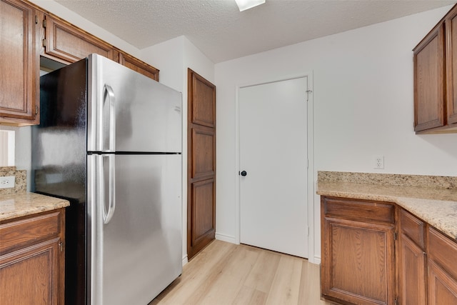 kitchen featuring light hardwood / wood-style floors, a textured ceiling, light stone counters, and stainless steel fridge