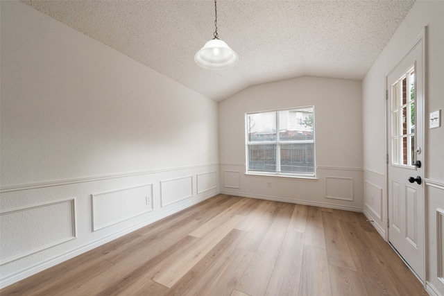 empty room with vaulted ceiling, light hardwood / wood-style flooring, and a textured ceiling