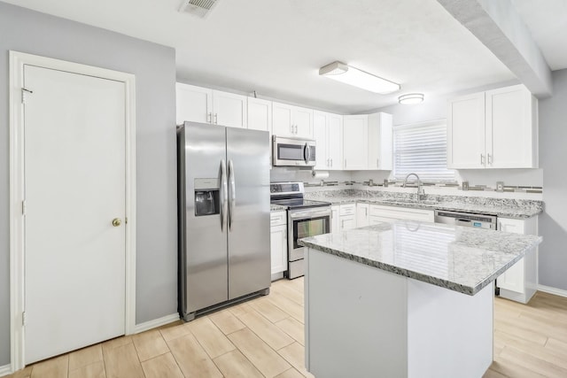 kitchen with white cabinetry, sink, stainless steel appliances, light stone counters, and a kitchen island