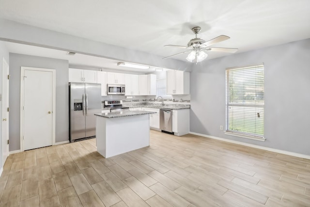 kitchen with light stone counters, stainless steel appliances, a kitchen island, sink, and white cabinetry