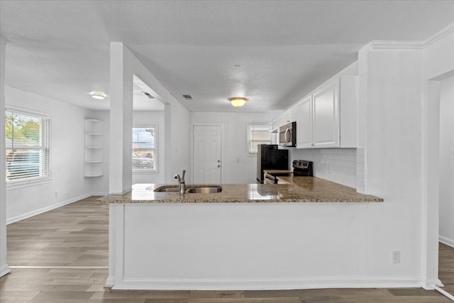 kitchen featuring kitchen peninsula, stainless steel appliances, sink, white cabinets, and light stone counters