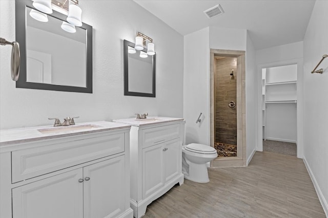 bathroom featuring vanity, tiled shower, hardwood / wood-style floors, and toilet